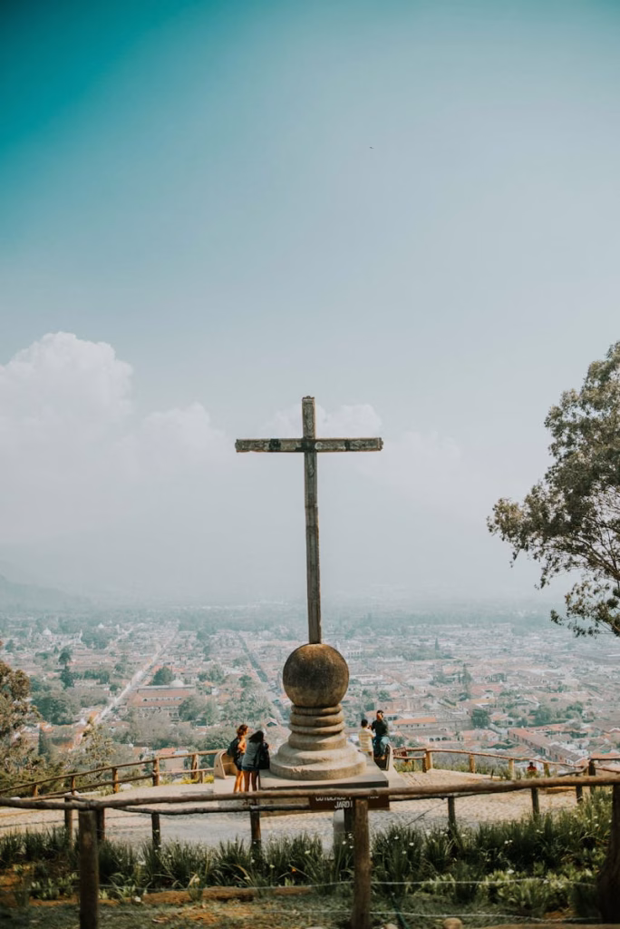 View from the Hill of the Cross overlooking Antigua Guatemala with a cross and people in the foreground.