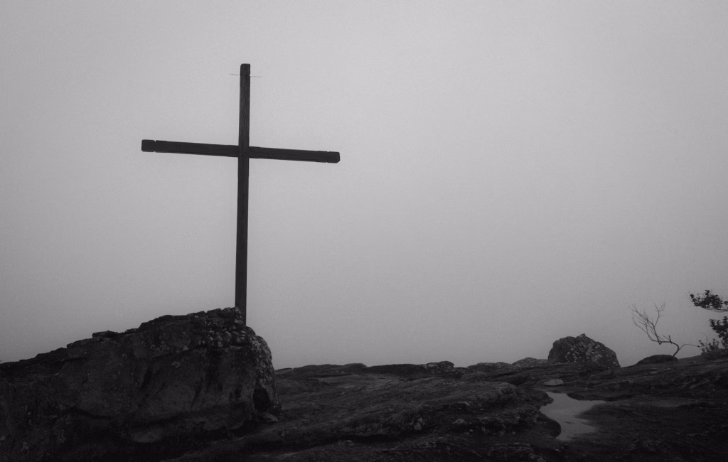 a black and white photo of a cross on a hill