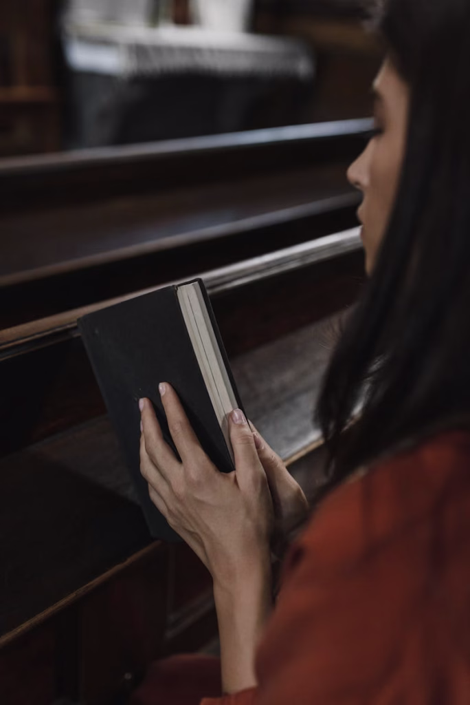 A woman in a church pew holding a book, absorbed in prayerful contemplation.